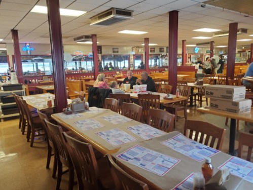 A spacious restaurant interior with wooden tables, menus on tables, and diners enjoying meals in a casual setting.
