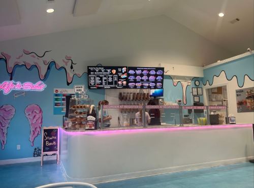 Bright ice cream shop interior with a colorful counter, menu screens, and a neon sign reading "Life is Sweet."