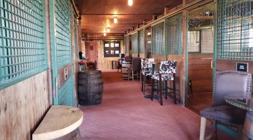 Interior of a rustic space with wooden walls, barrel tables, and cow-print chairs, featuring a cozy, inviting atmosphere.