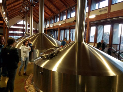 A brewery interior featuring large stainless steel brewing tanks and visitors exploring the space.