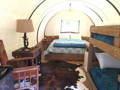 Cozy interior of a glamping tent featuring a double bed, bunk beds, and rustic furniture.