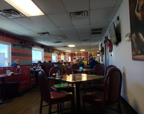 A cozy restaurant interior with red booths, tables, and patrons enjoying their meals. Walls decorated with art.