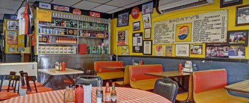 A cozy diner with red and white checkered tables, colorful walls, and a vintage soda display.