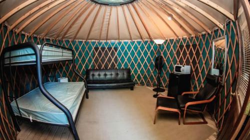Interior of a yurt featuring a bunk bed, a black sofa, chairs, and a microwave against a colorful patterned wall.