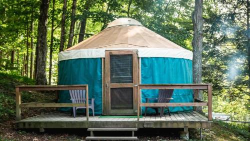 A cozy yurt with a wooden deck, surrounded by trees, featuring two chairs in front.