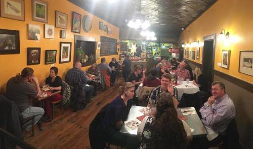 A cozy restaurant interior with diners at tables, colorful walls adorned with artwork, and warm lighting.