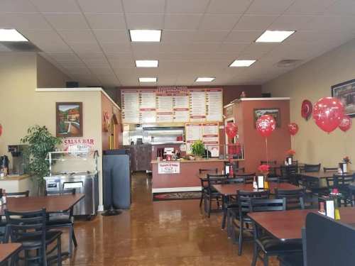 Interior of a casual dining restaurant with tables, a salsa bar, and a menu board on the wall, decorated with balloons.