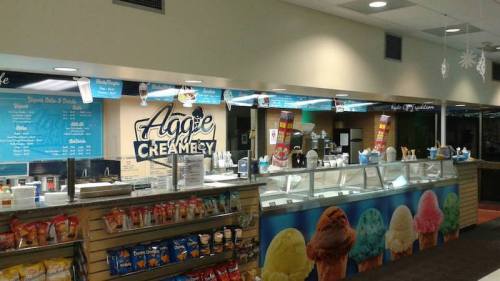 A colorful ice cream shop counter with various flavors, snacks, and a menu displayed on the wall.