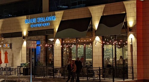 Exterior of Blue Island Oyster Bar at night, featuring illuminated signage and outdoor seating with string lights.