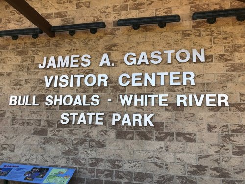 Sign for James A. Gaston Visitor Center at Bull Shoals-White River State Park, featuring stone wall background.