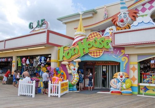 Colorful entrance to a funhouse with clown decorations, surrounded by people and carnival-themed items.