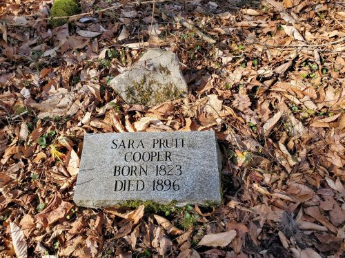 Gravestone of Sara Pruitt Cooper, born 1823, died 1896, surrounded by fallen leaves.