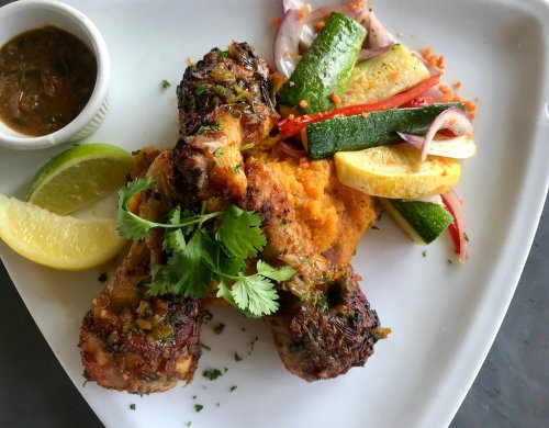 Grilled chicken drumsticks on a bed of mashed sweet potatoes, served with sautéed vegetables and lime wedges.