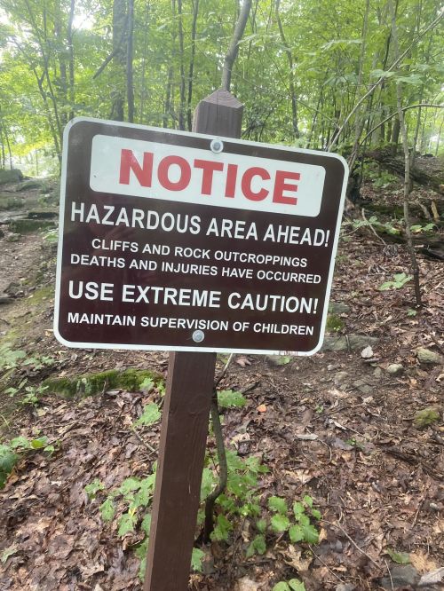 Sign warning of hazardous area ahead, advising caution due to cliffs and rock outcroppings; supervision of children required.
