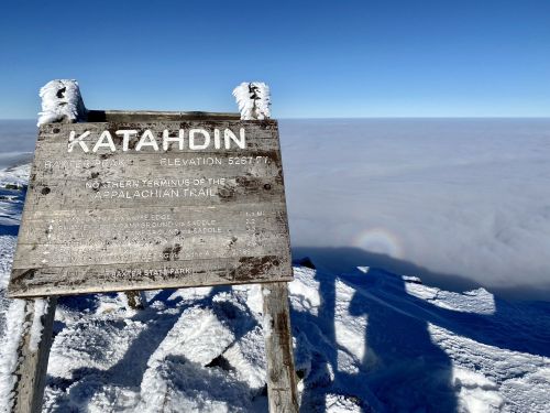 A snowy sign at Katahdin, elevation 5,267 feet, above a sea of clouds, marking the northern end of the Appalachian Trail.