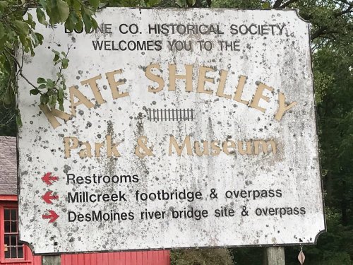 Sign for Kate Shelley Park & Museum, listing restrooms, Millcreek footbridge, and Des Moines river bridge site.