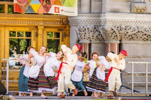 Children in traditional costumes perform a lively dance on stage, showcasing cultural heritage and joy.