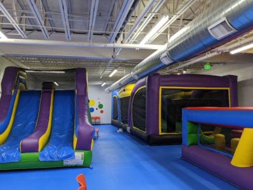 Indoor play area featuring colorful inflatable slides and bounce houses on a blue floor.