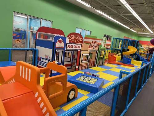 Colorful indoor play area with toy buildings like a restaurant and post office, featuring slides and play vehicles.