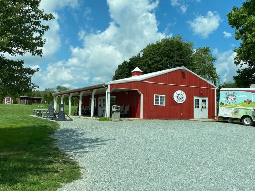 A red barn-style building with a white roof, surrounded by green grass and trees, under a partly cloudy sky.