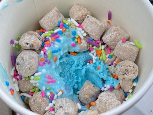 A cup filled with blue ice cream, cookie dough bites, and colorful sprinkles.