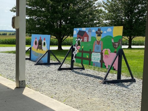 Two colorful farm-themed signs featuring cartoon animals and a barn, set against a green field and blue sky.