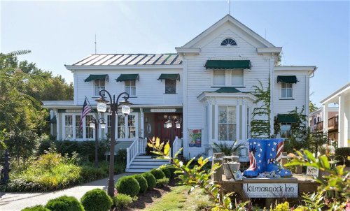 A charming white inn with green awnings, surrounded by well-kept gardens and decorative signage.