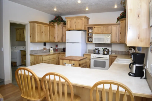 A spacious kitchen with wooden cabinets, a white refrigerator, and a countertop with three wooden chairs.