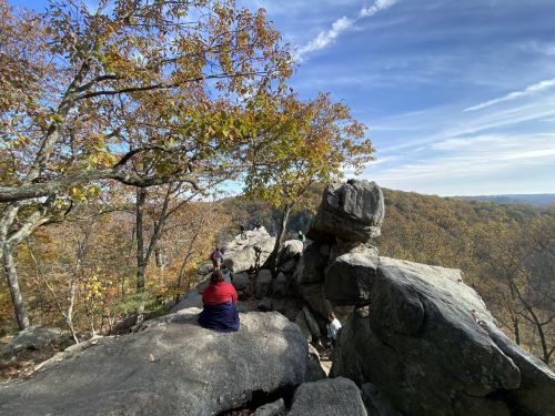 A scenic view from a rocky outcrop, with people sitting and enjoying the autumn foliage in the background.