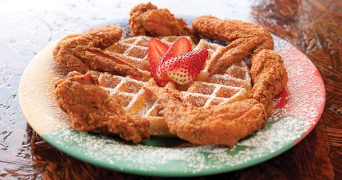 A plate of waffles topped with fried chicken wings and strawberries, dusted with powdered sugar.