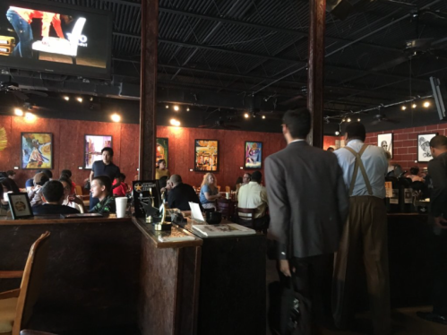 A busy restaurant interior with patrons dining and chatting, featuring artwork on the walls and a lively atmosphere.