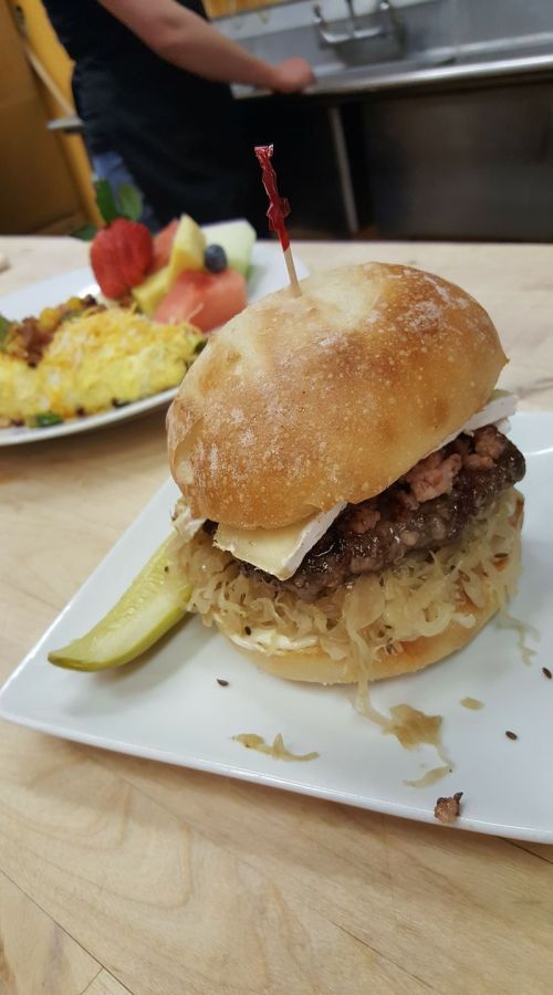 A close-up of a sandwich with meat, cheese, and sauerkraut on a plate, garnished with a pickle and a toothpick.