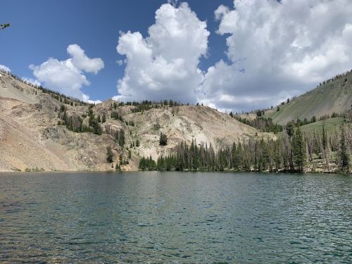 A serene lake surrounded by mountains and lush trees under a partly cloudy sky.