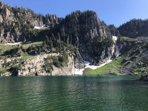 A serene lake surrounded by steep, rocky mountains and lush greenery under a clear blue sky.