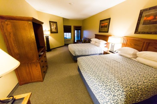 A cozy hotel room featuring two beds, a wooden dresser, and warm lighting.