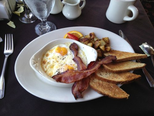 A plate with fried eggs, crispy bacon, toast, and seasoned potatoes, served with orange and apple slices.