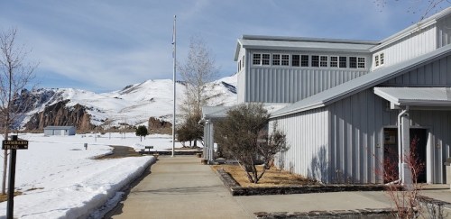 A snowy landscape with a modern building and mountains in the background, under a clear blue sky.