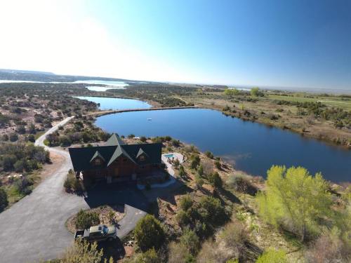 Aerial view of a lakeside cabin surrounded by greenery and water under a clear blue sky.