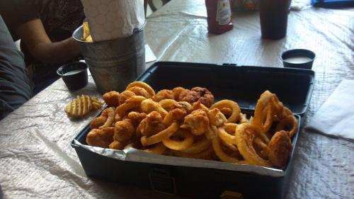 A box filled with crispy onion rings and fried chicken, accompanied by dipping sauces on a table.