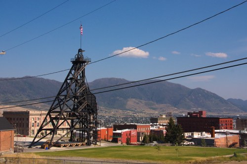 A mining structure stands against a backdrop of mountains and a small town under a clear blue sky.