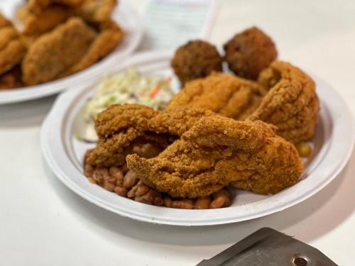 A plate of fried catfish with coleslaw, baked beans, and hushpuppies on a white paper plate.