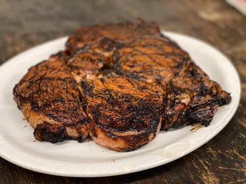 A perfectly cooked, charred ribeye steak on a white plate, resting on a rustic wooden table.