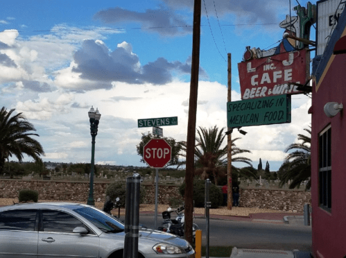 A street view featuring a café sign, palm trees, and a stop sign under a cloudy sky.