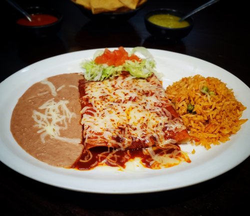 A plate of enchiladas topped with cheese, served with rice, refried beans, lettuce, and tomato.