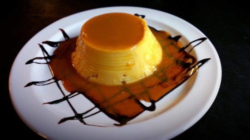 A creamy flan topped with caramel sauce, served on a white plate with chocolate drizzle.