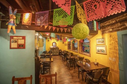 Colorful decorations hang from the ceiling of a cozy restaurant with empty tables and a warm, inviting atmosphere.