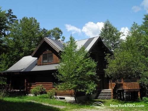A rustic wooden cabin surrounded by trees under a blue sky with fluffy clouds.