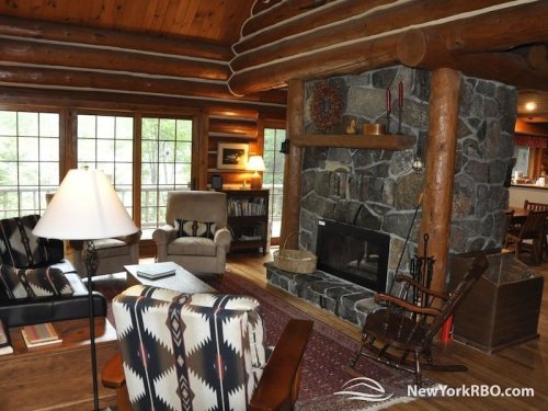 Cozy log cabin interior featuring a stone fireplace, comfortable seating, and large windows for natural light.