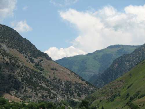 A scenic view of green mountains under a partly cloudy sky, showcasing rugged terrain and natural beauty.