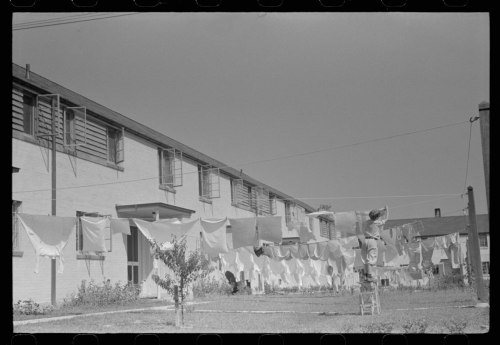A row of white laundry hanging on a line in front of a residential building under a clear sky.